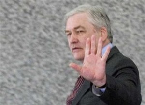 Conrad Black stands in front of granite wall with one hand up. Copyright bildungblog.blotspot.com 2010